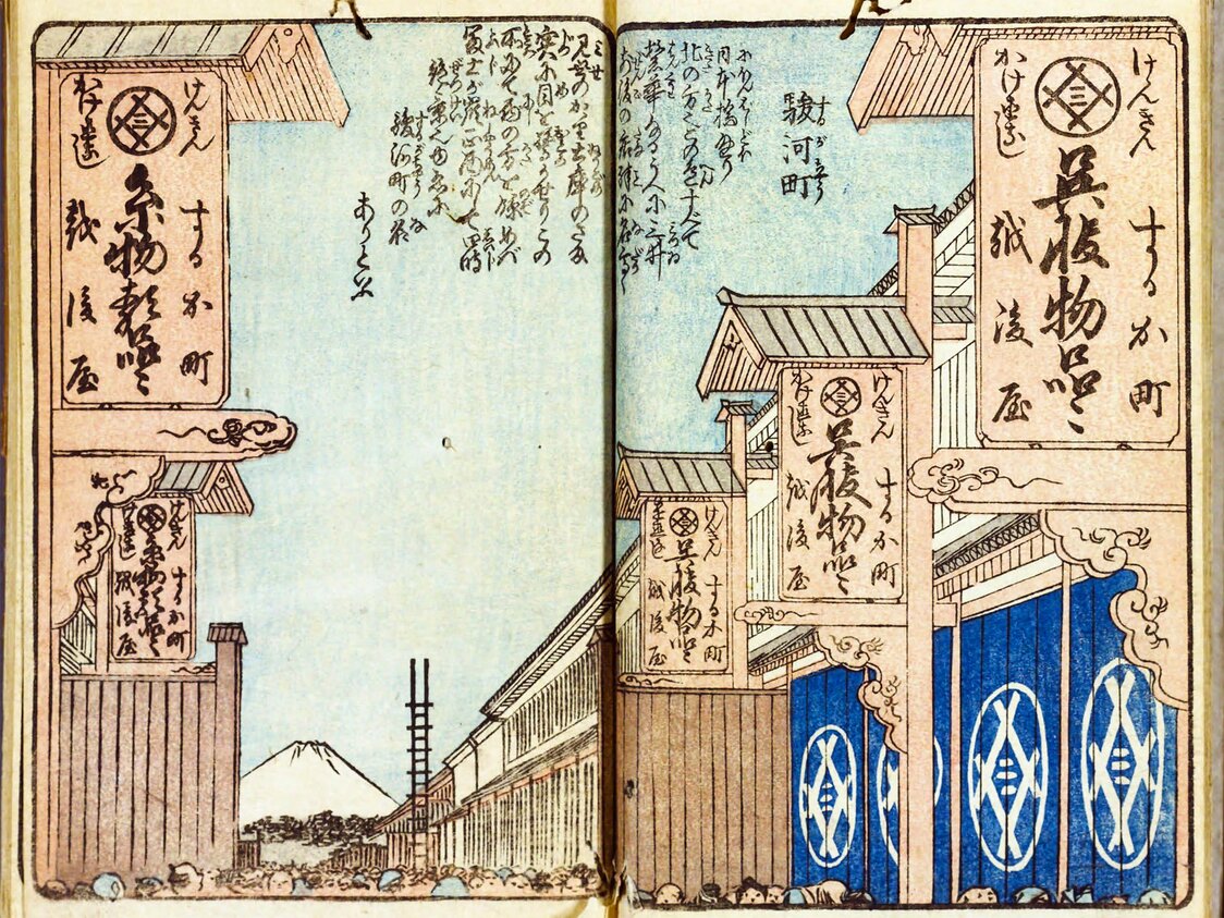 広重作『絵本江戸土産』の5編にある「駿河町」（1854頃刊　国会図書館所蔵）。街並み、富士の位置や大きさなどが、写実的に描かれている。看板を見ると、この時代の越後屋は、右が呉服物品（絹織物）、左が糸物物品（木綿、麻など）と分かれていたようだ