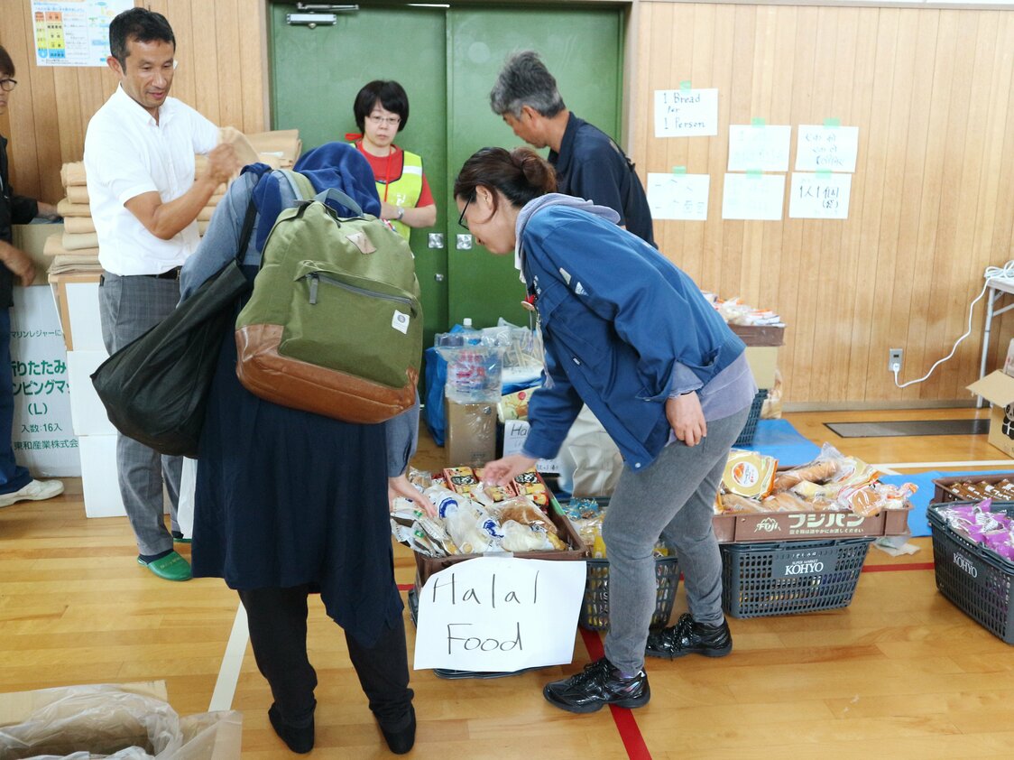 箕面市某所小学为大阪北部地震的避难所，外国人占多数。市政府工作人员正在对清真食品进行说明（2018年6月20日，时事社）