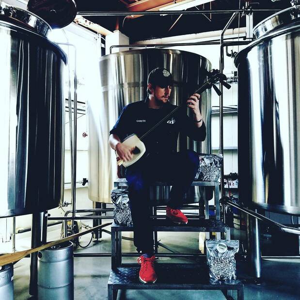 Burns playing Tsugaru-jamisen surrounded by beer fermentation tanks. (Courtesy of Gareth Burns)