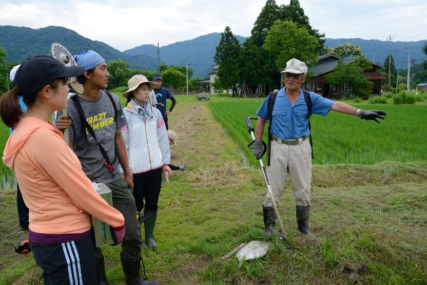 水田での水の管理方法を農家の人から教わる若者たち