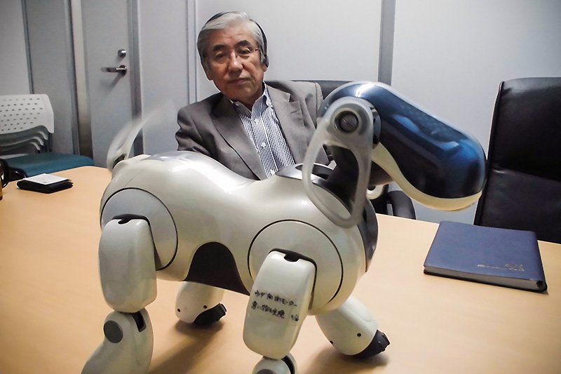 Норимацу Нобуюки смотрит на робота AIBO, машущего хвостом