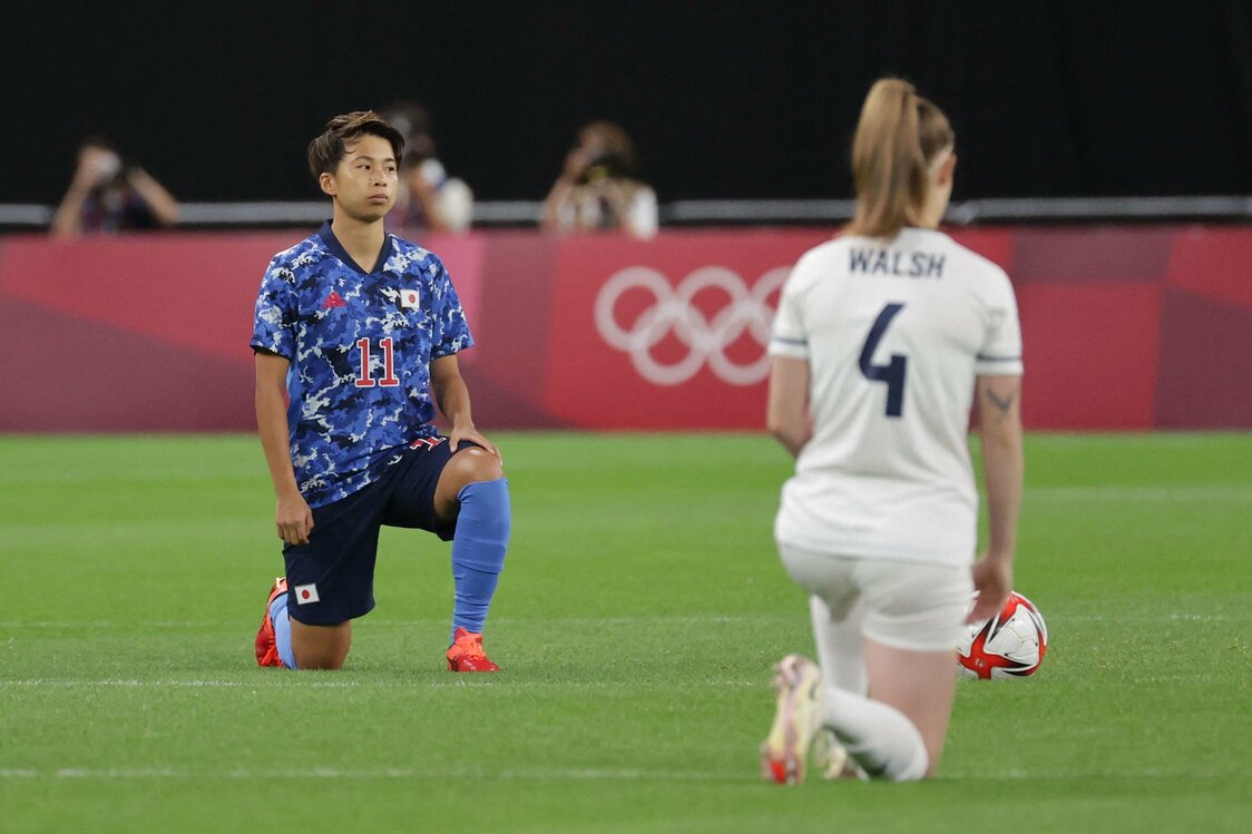 試合前に片膝をついて人種差別への抗議を示す、サッカー女子日本代表の田中美南（みな／左）とイギリスの選手（2021年7月24日、北海道・札幌ドーム） AFP＝時事