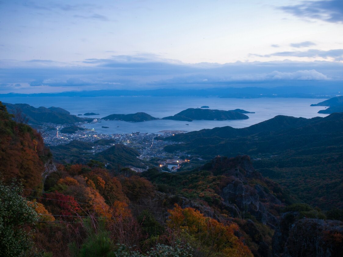 Atardecer sobre el mar Interior de Seto. Destacan en la imagen las hojas rojas de la montaña y las luces en las inmediaciones del puerto de Kusakabe.