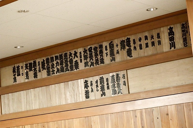 Placa con los nombres del establo de Takadagawa, escritos por Shikimori Kandayū. Los miembros del establo son el oyakata, los veinte luchadores, dos gyōji y un tokoyama. (La clasificación de los luchadores corresponde a la de mayo de 2018.)