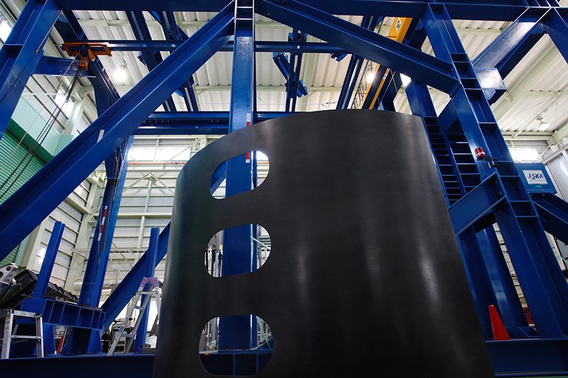 En JAXA se están llevando a cabo estudios para garantizar un determinado nivel de resistencia, con el motivo de obtener las certificaciones necesarias. El panel negro de esta carcasa azul, utilizada en pruebas de verificación de solidez vital, está construido con el mismo material CFRP empleado en los fuselajes de avión.