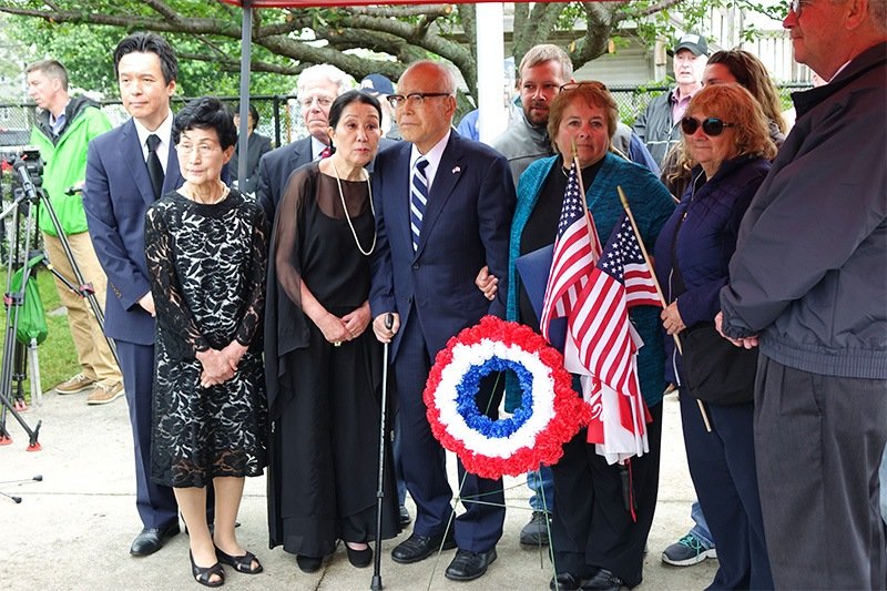 Mori Kayoko (second from left), Mori Shigeaki (center), and Normand Brissette’s niece Susan Brissette Archinski (behind flags), with members of the POWs’ families and friends, stand for the dedication of a memorial tablet to Normand Brissette.