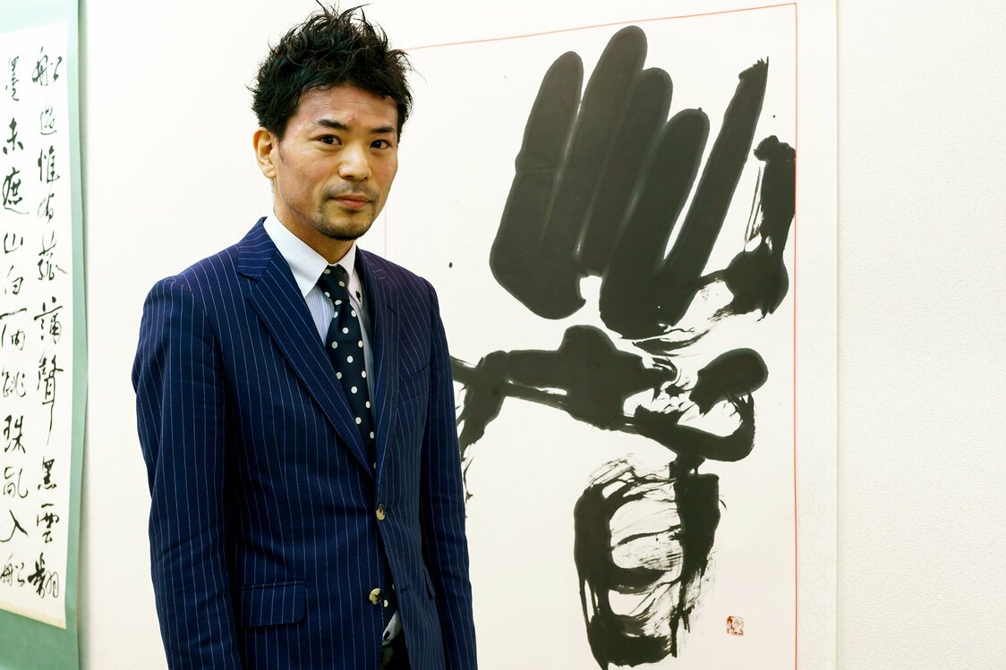 Miyazaki stands in front of his own work 著 (cho, ichijirushii), meaning “remarkable,” written in the reisho style.