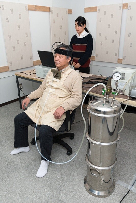 森林アロマを吸い込んだ被験者の、脳の前頭前野の活動を測定する実験の様子。宮崎研究室の池井晴美研究員（後方）も実験に協力。