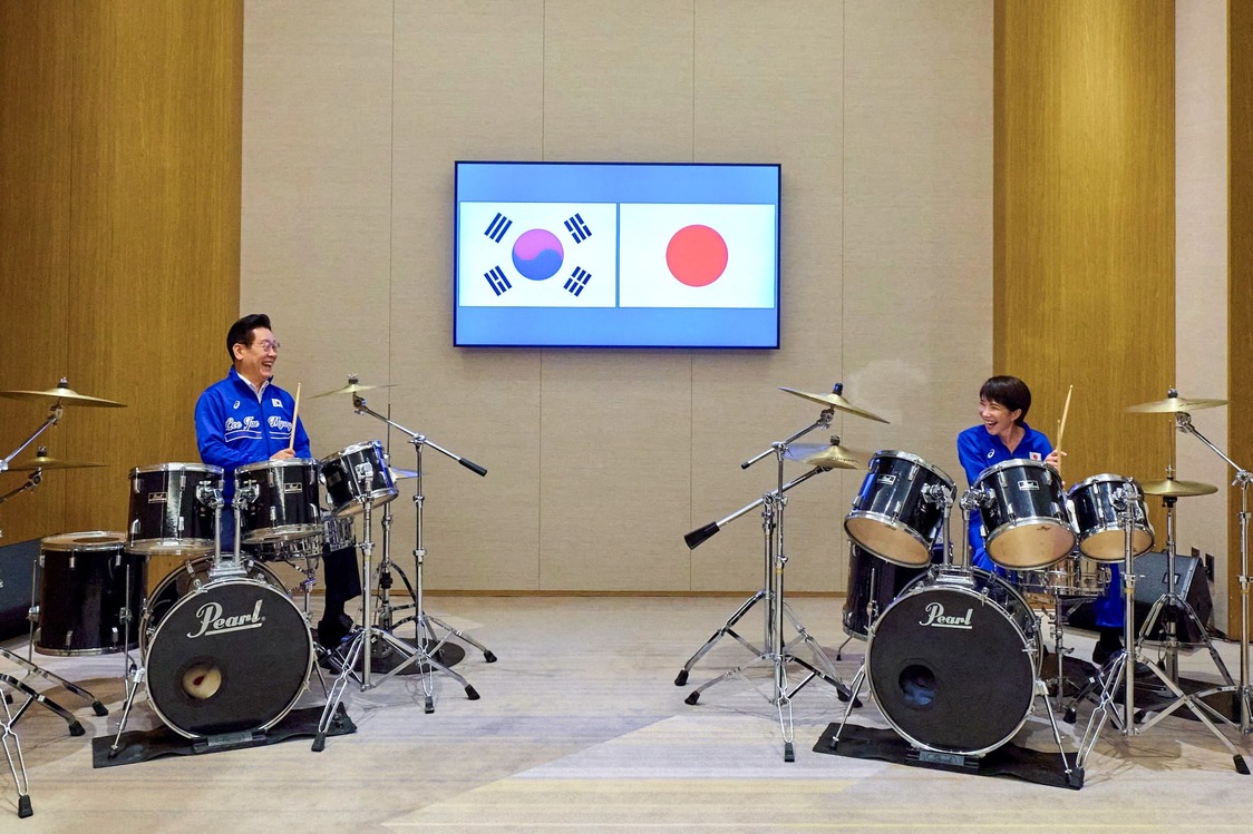 Prime Minister Takaichi (right) and President Lee play drums together following their meeting. (© Yonhap/Reuters)