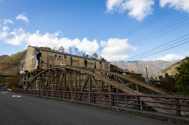 The iron truss Furukawa Bridge (foreground), an important cultural property, spans the Matsuki River, a tributary of the Watarase River. The old Honzan smelter stands idle in the background.