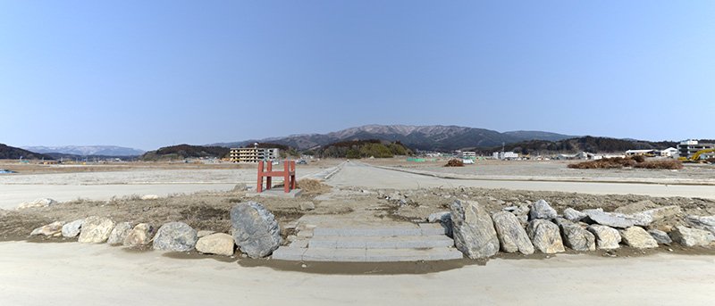 がれきが片づけられ、「更地」が広がる陸前高田の旧中心市街地。後方中央に見える小山が「高田城」跡。手前のJR陸前高田駅前広場跡には、ロータリーに設置されていたモニュメントの骨組みの一部だけが残されていた。