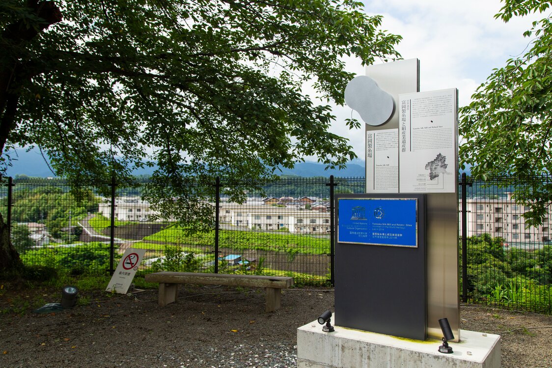 ブリュナ館の裏庭にある「世界遺産登録記念銘」。フェンスの向こうには鏑川（かぶらがわ）が流れ、工場で使用する水の心配もなかった
