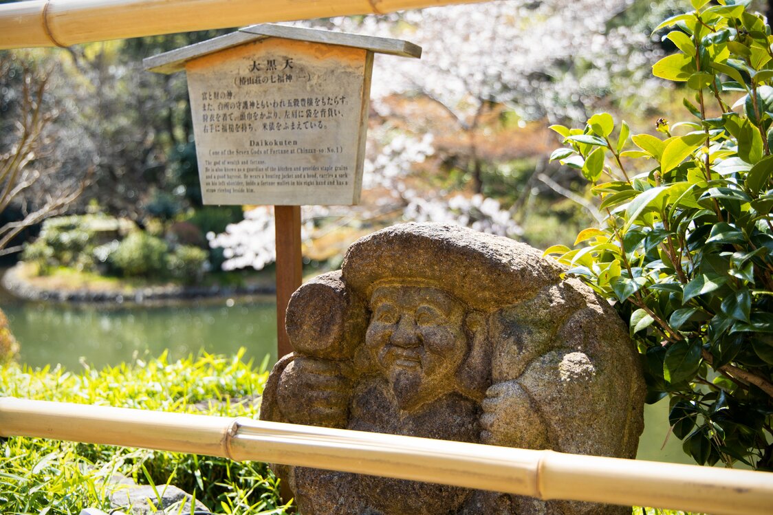 Une statue de pierre Daikokuten, l’un des Sept Dieux de la Chance, associée à la richesse et à la prospérité. Les statues des Six autres Dieux de la Chance parsèment çà et là les allées du jardin. Nombreux sont les visiteurs qui s’amusent à les chercher et à les prendre en photo.