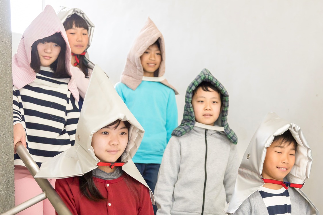 学生戴着防灾头套参加地震避难演练（PIXTA）