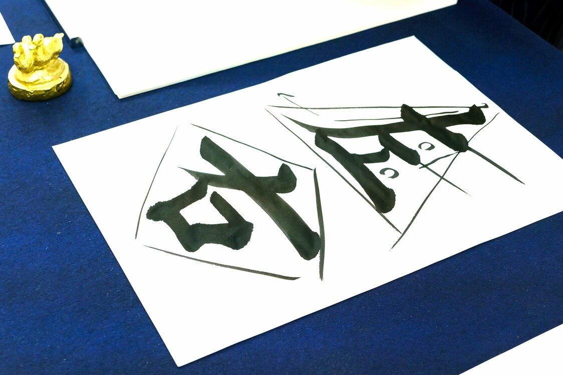 The teacher uses geometric shapes to highlight the ideal balance of the kanji: a triangle for 左 (hidari, meaning “left”) and a diamond for 右 (migi, “right”). Additional lines and small circles are guides to appropriate stroke placement and empty spaces.