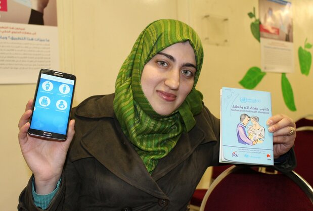 紙製の母子手帳と母子手帳アプリをダウンロードしたスマートフォンを手にするパレスチナ難民キャンプで暮らすラワン・フセインさん（2017年4月4日＝ヨルダンのアンマンにある国連パレスチナ難民救済事業機関（UNRWA）の診療所）。難民の間では母子手帳が「命のパスポート」と呼ばれることも（時事）