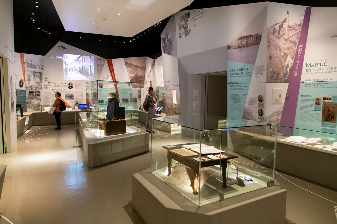 複雑な凹凸を描く斬新なデザインの壁に、分かりやすい解説パネルが並ぶ第1展示室。ガラスケースには直筆原稿や旅行かばんなどの遺品が置かれる