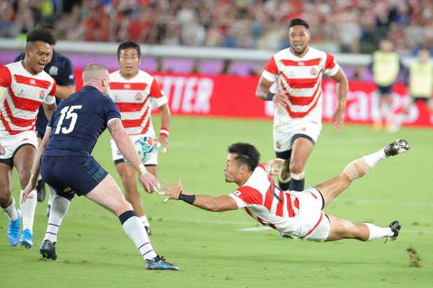 Fukuoka Kenki delivers an acrobatic offload pass to Matsushima, who carries it past the line for Japan’s first try against Scotland on October 13 in Yokohama. (© Jiji)