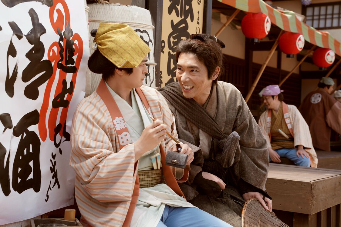 Sōichirō se acerca a Ichihachi (Seto Kōji, a la izquierda), kidogeisha del Morita-za. (© 2026 Comité de Producción de Kobikichō no adauchi © 2023 Nagai Sayako / Shinchōsha)