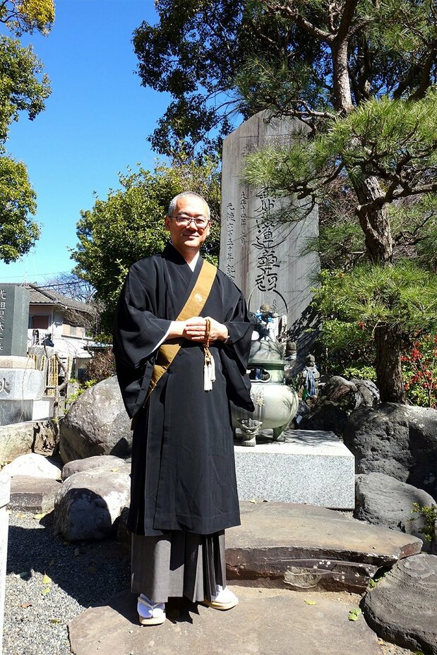 供養塔の前に立つ服部功志住職(筆者撮影)