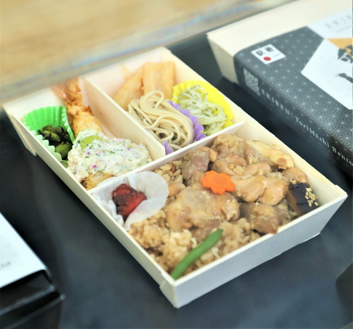 秋田のグルメを盛り合わせた「秋田弁当」は、県から委託を受けて開発した新商品。田楽味噌を塗ったきりたんぽ、稲庭うどん、いぶりがっこなどが添えられている。　写真提供：花善