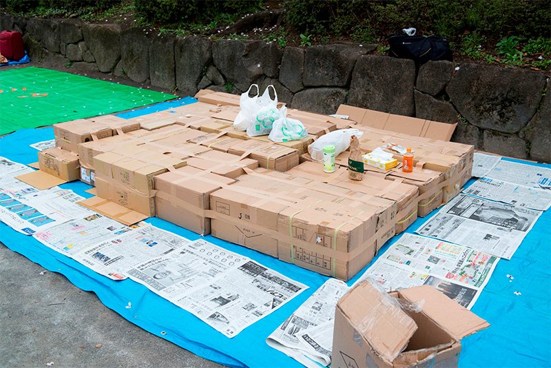 La omnipresente lona azul, una mesa hecha con cajas de carton y periódicos en los que se sentarán los comensales durante el hanami.
