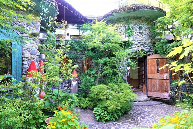 あじさい山から徒歩15分ほどに立地。鯉やチョウザメが泳ぐ、石畳のアプローチを抜けて館内に入ると、淡い照明の中に幻想的な世界が現れる。テラス付きカフェのテーブルや椅子も友永さんの手づくりで、池を泳ぐ鯉を眺めながらゆっくりとくつろげる 撮影:天野久樹