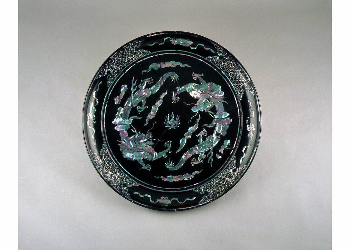 Bandeja de laca negra con incrustaciones de nácar formando nubes y dragones. Datada entre los siglos XVIII y XIX. En el centro de la bandeja, los dragones portando la mítica piedra chintamani y la nube irisada de los buenos auspicios, elementos ambos de la tradición budista. (Colección del Museo de Arte de Urasoe)