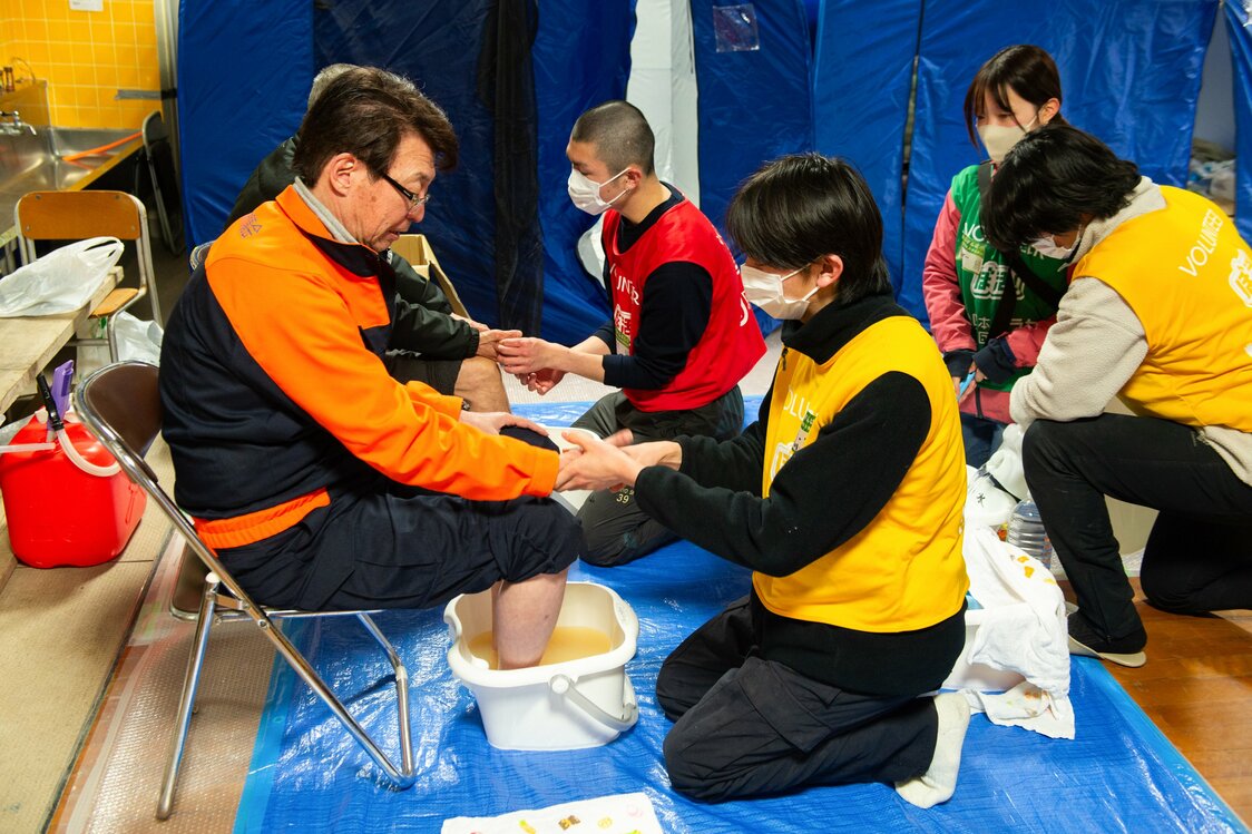 足湯を受けた浦秀一市議会議員（左）は「地割れしたデコボコ道を3カ月近く歩き回っているから、足がボロボロ。今日は足を温めたから、ぐっすり眠れるよ」と笑顔で語った