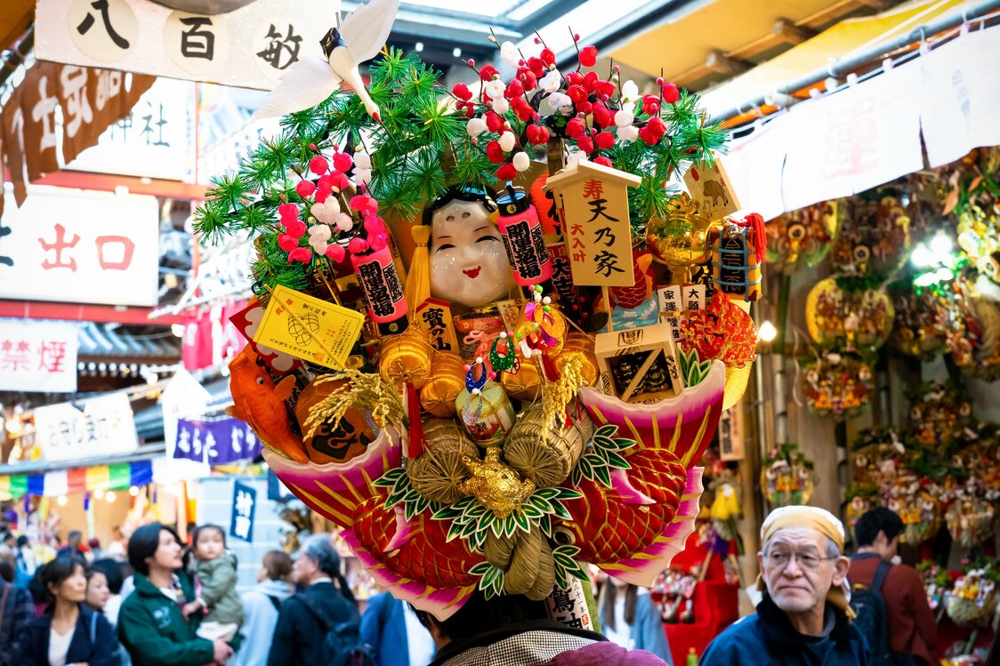 大きな熊手を持ち帰る参拝客。おかめや鶴亀、米俵などの縁起物がぎっしりと飾られている