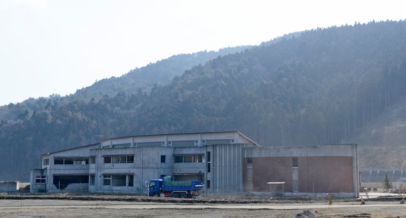 津波で多くの児童と教員が亡くなった石巻市立大川小学校。土砂やがれきを積んだダンプカーが校舎跡の横を通り過ぎる。