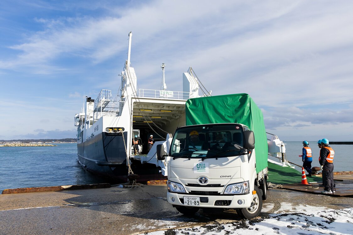 Les camions chargés d’aide humanitaire débarquent les uns après les autres dans le port d’Iida. L’absence de manœuvre de transbordement de marchandises leur permet de se diriger immédiatement chacun vers leur destination, là où l’aide est directement nécessaire.