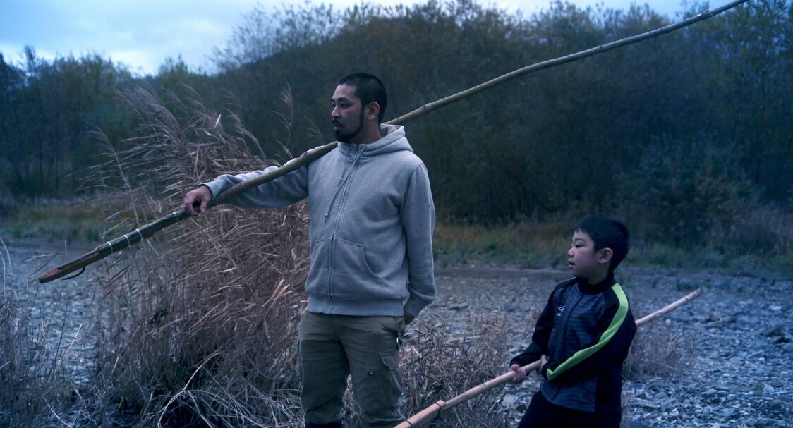 Shige lleva a Motoki a pescar, con un marep al hombro. (© 2024 Takeshi Fukunaga/AINU PURI Production Committee)