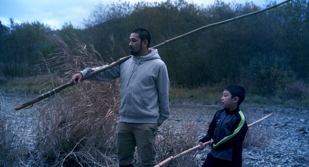 Shige lleva a Motoki a pescar, con un marep al hombro. (© 2024 Takeshi Fukunaga/AINU PURI Production Committee)