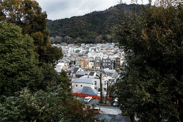 Vista panorámica desde el oeste de la Maison O (diseñada por Nakayama Hideyuki, 2009). El edificio se alza rozando con la valla de color bermellón que rodea el santuario.