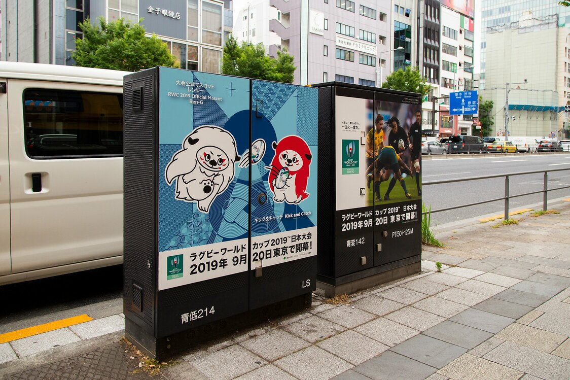 歩道の配電地上機器を飾るラグビーW杯のポスター。公式マスコット「レンジー」の背景にも、ユニティグラフィックが使われている