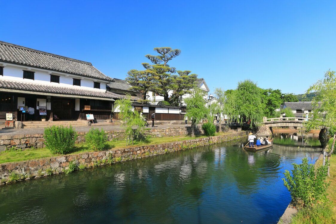 Una barca navega por un canal en el distrito histórico de Kurashiki. (© Pixta)