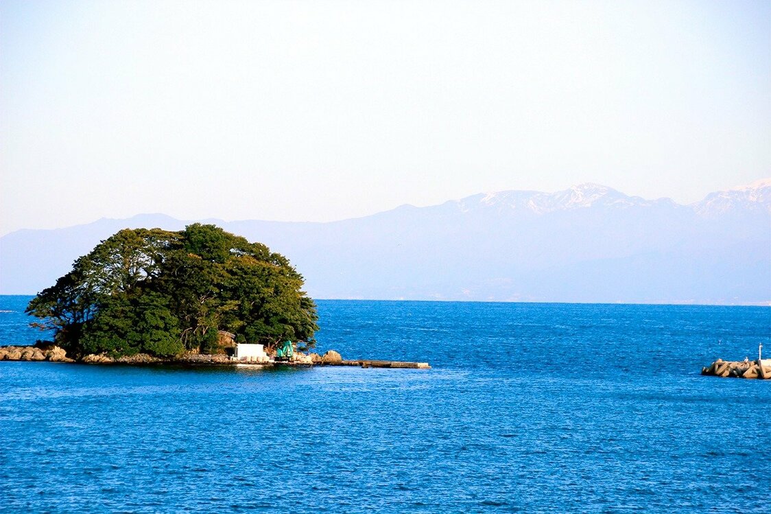 湾岸サイクリングコース沿いから望んだ富山湾に浮かぶ唐島と立山連峰。氷見市・比美乃江公園にて（筆者撮影）