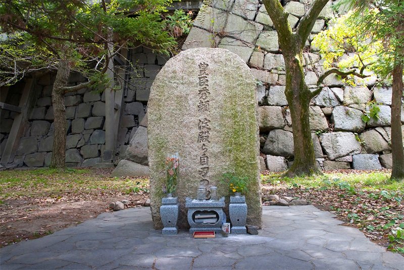 Sobre el fondo de las grandes piedras que cimientan el castillo, la lápida de piedra que señala el lugar donde se suicidaron Hideyori (hijo de Hideyoshi) y su madre, Yodo-dono.