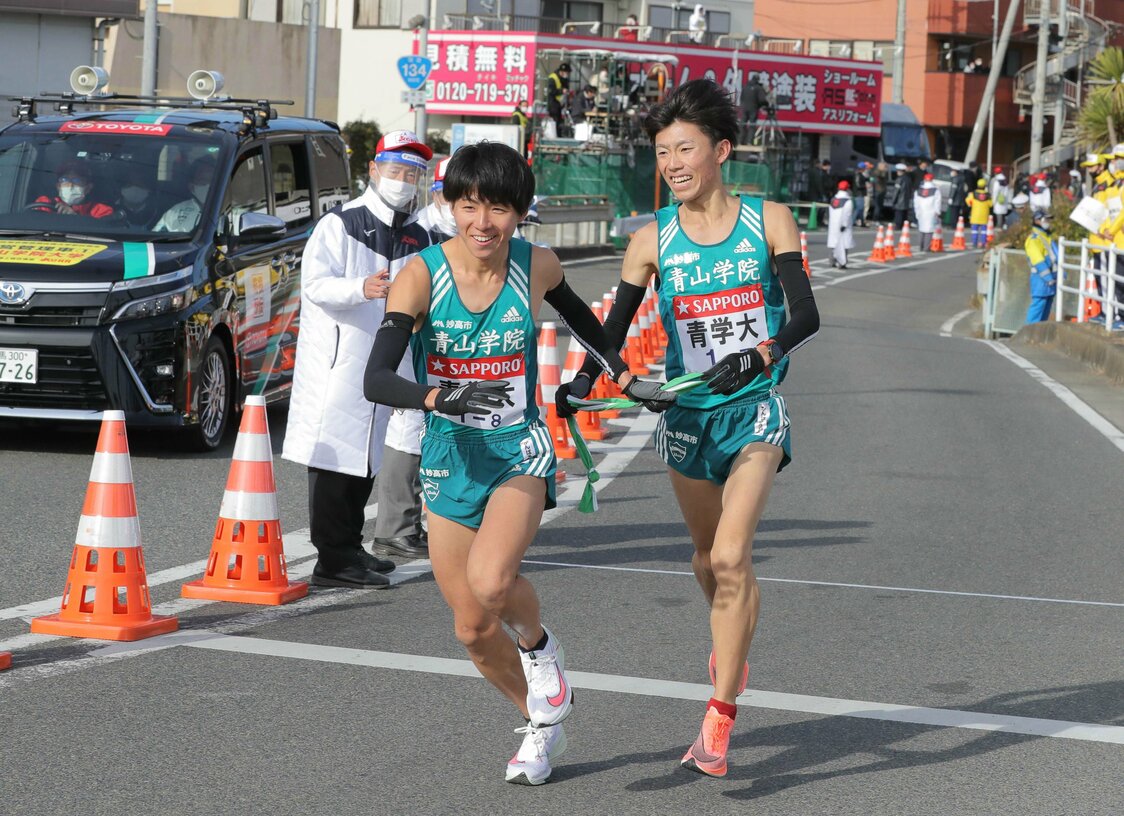 第97届“箱根驿传”，青山学院大学跑第7区间的近藤幸太郎（右）与跑第8区间的岩见秀哉在平冢交接点交接肩带。青山学院大学近年来称霸“驿传”界，选手的笑容令人印象深刻（2021年1月3日，神奈川县平冢市，时事社）