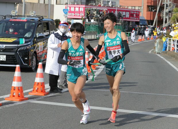 第97届“箱根驿传”，青山学院大学跑第7区间的近藤幸太郎（右）与跑第8区间的岩见秀哉在平冢交接点交接肩带。青山学院大学近年来称霸“驿传”界，选手的笑容令人印象深刻（2021年1月3日，神奈川县平冢市，时事社）
