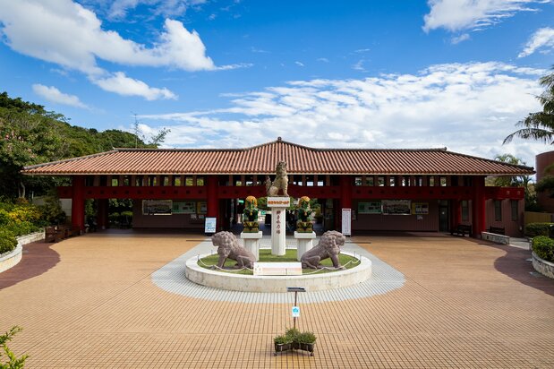 The entrance of Okinawa World features a traditional red-tiled roof and the Shishiku-no-Tō monument displaying Okinawa’s lion-like shīsa.