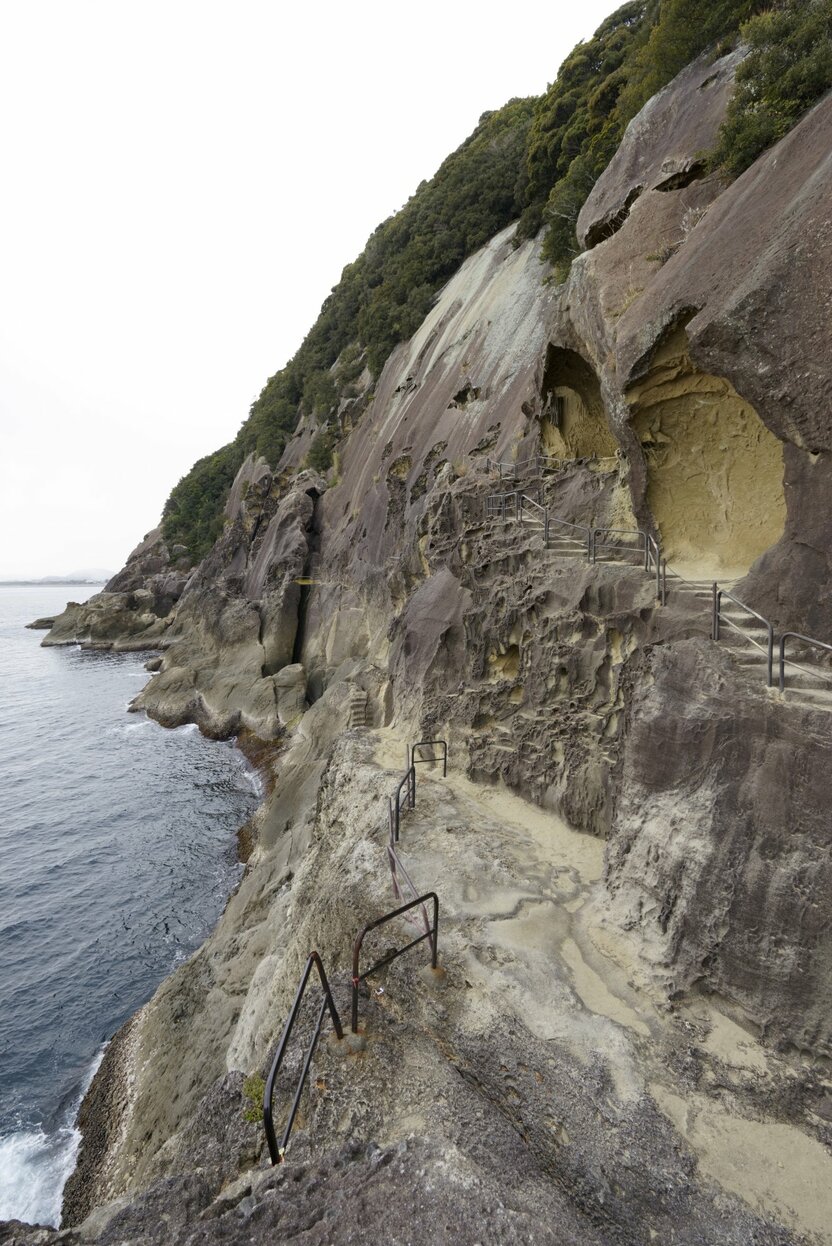 The footpath from the west of the Senjōjiki Cave traverses a steep and narrow stretch of rugged coastline, where waves pound against the bottom of the rocky cliff. (© Ōsaka Hiroshi)