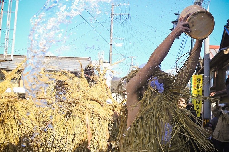 Des hommes en costume de paille et jetant de l’eau autour d’eux (Photo avec l’aimable autorisation de la ville de Tome)