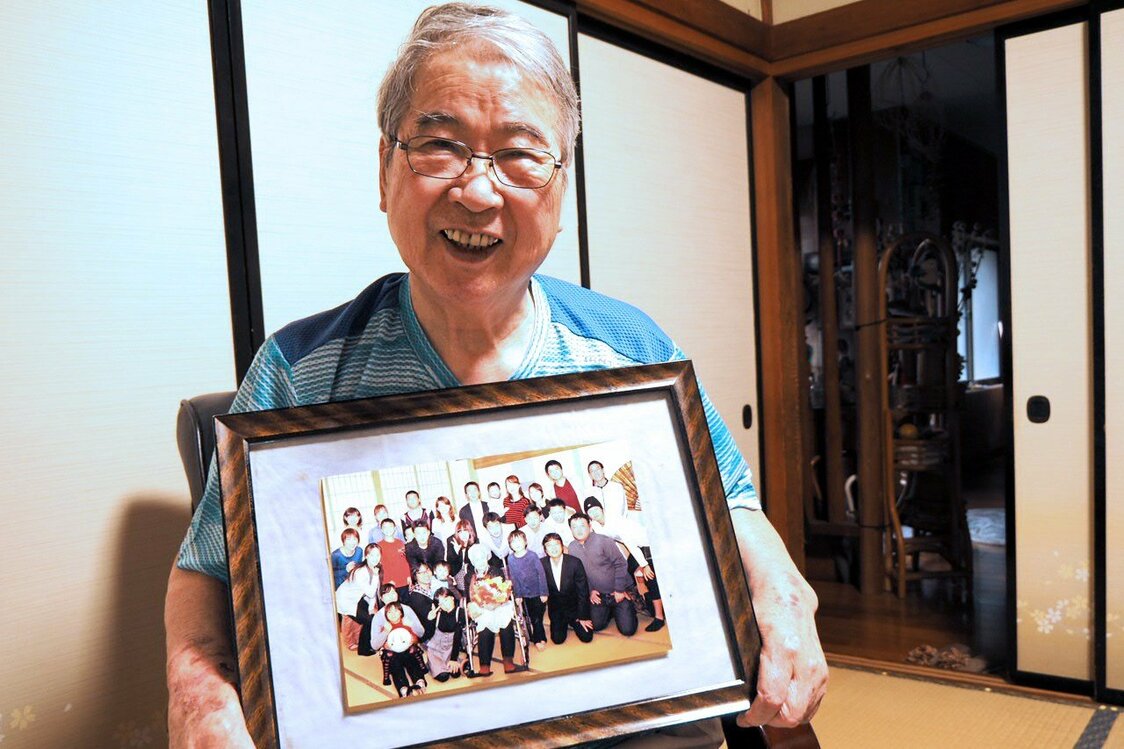 市川英雄手上拿着全家福照片，照片上一大家子围绕在老太太的身边