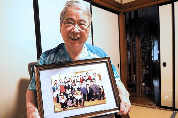 市川英雄手上拿着全家福照片,照片上一大家子围绕在老太太的身边