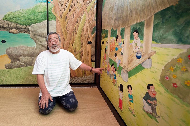 Kitami nos cuenta sus recuerdos mientras mira a la pintura. A su espalda el laurel de Indias.