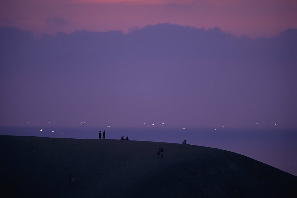 夕暮れに浮かび上がる砂丘のシルエットの奥にいさり火が見える　写真提供：鳥取県