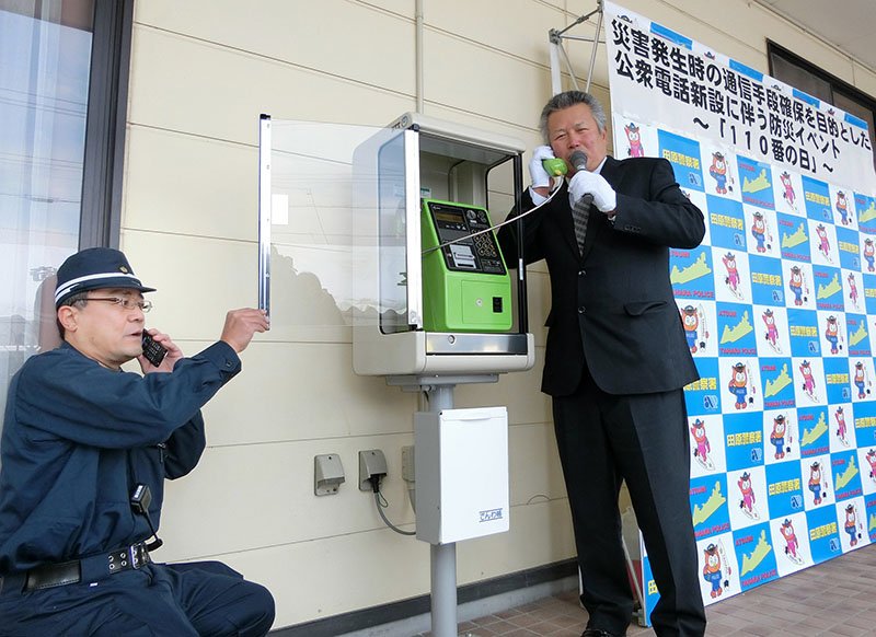 在集会所公用电话开通仪式上模拟拨打110报警的当地居民（时事社）
