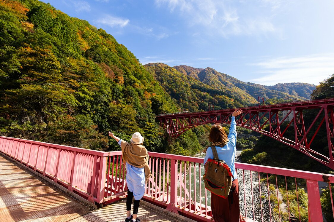 Dos mujeres en el puente de Yamabiko saludan al tren que pasa por el puente de Shin-Yamabiko.